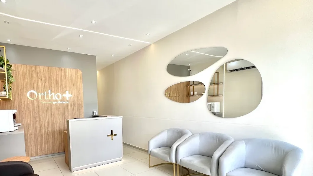 Sala de espera da Orthomais, com poltronas claras de base dourada, espelhos decorativos e balcão de recepção.